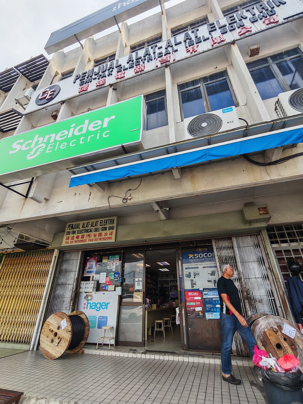 Four-storey shoplot with a green Schneider Electric sign and a Chi-Tak Electrical signboard, cable drums and a Hager display at the shop entrance