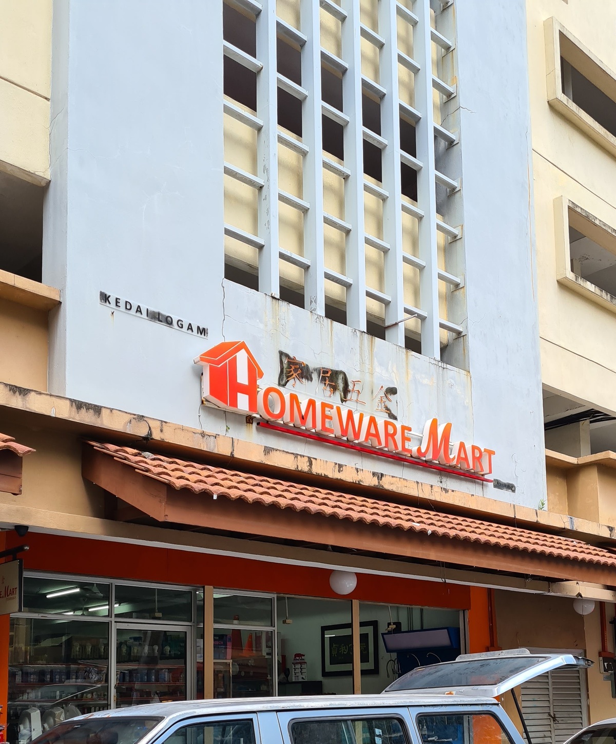 Ground-floor glass shopfront under a tiled awning with an orange HOMEWARE MART sign and Chinese characters on the wall above, in a cream apartment block