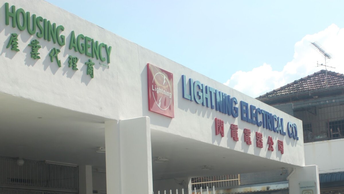 White building fascia with a red Lightning logo and blue Lightning Electrical Co. lettering beside a green Housing Agency sign