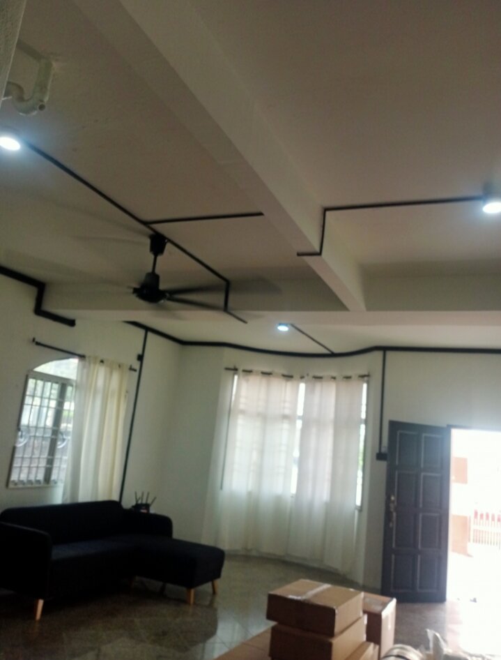 Living room with black surface conduit running across the ceiling to a ceiling fan and downlights, a sofa and boxes on the floor