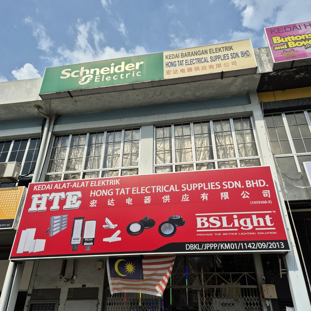 Two-storey shop with a green Schneider Electric signboard on top and a red Hong Tat Electrical Supplies banner with BSLight lamp pictures over the entrance