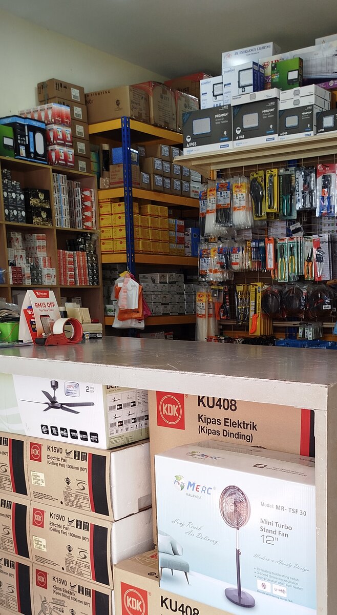 Shop counter stacked with fan boxes, in front of shelves of boxed floodlights and LED bulbs and a pegboard of cable ties and pliers