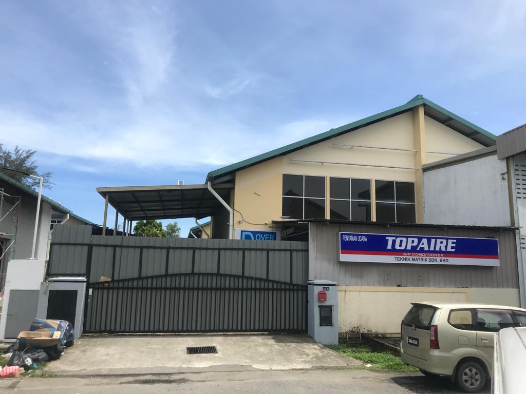 Industrial building with a gabled roof and upper windows behind a gate, with a blue and red Topaire Air Conditioner sign naming Teknik Matrix Sdn Bhd