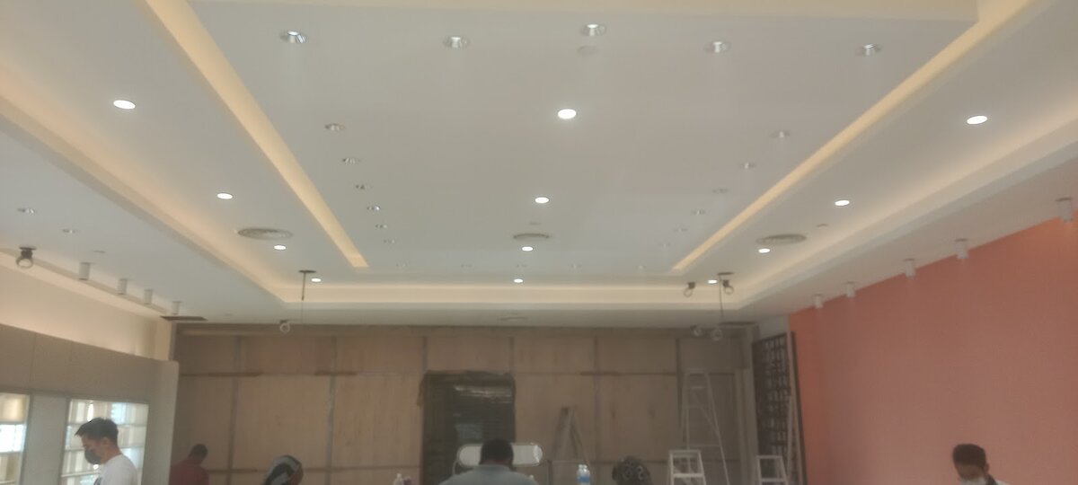 Empty shop with a white stepped ceiling, recessed downlights and cove lighting, and workers at the back