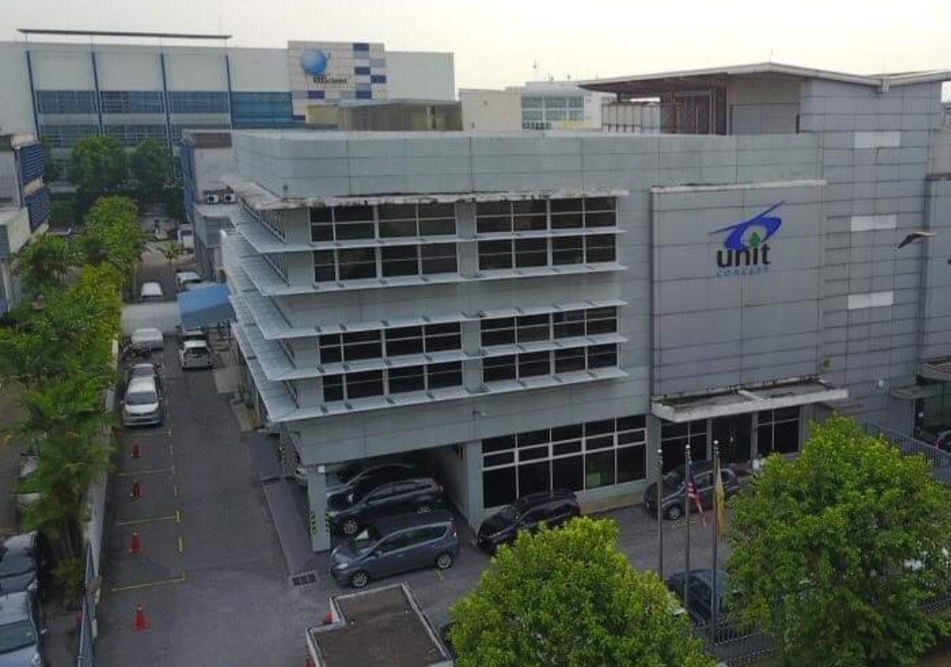 Grey four-storey office and factory building with the Unit Concept logo, car park and trees in front