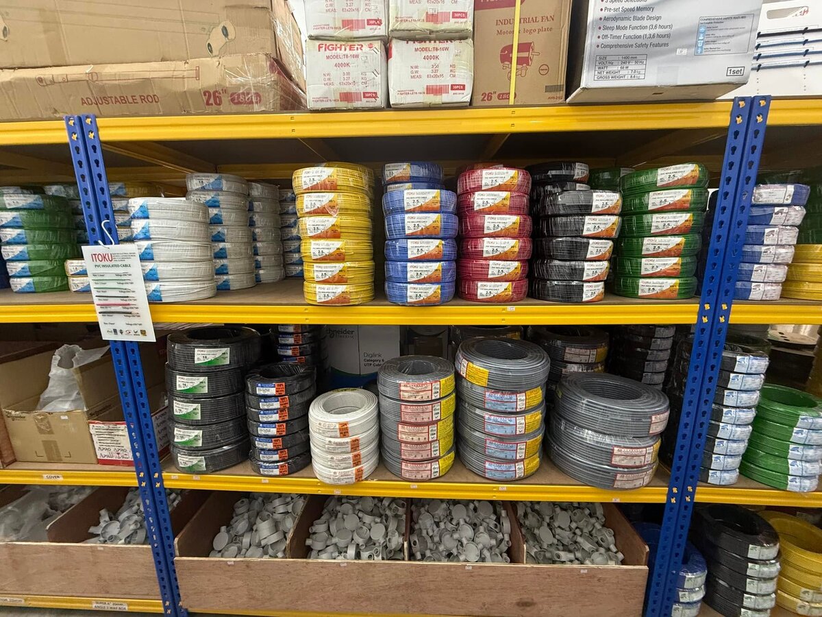 Yellow and blue warehouse racks stacked with coils of yellow, blue, red, black, green, white and grey electrical cable above bins of grey conduit boxes