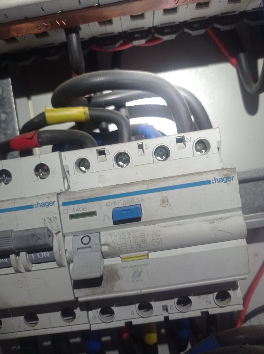 Close-up of a grey Hager four-pole residual-current circuit breaker with a blue test button, cables entering from above