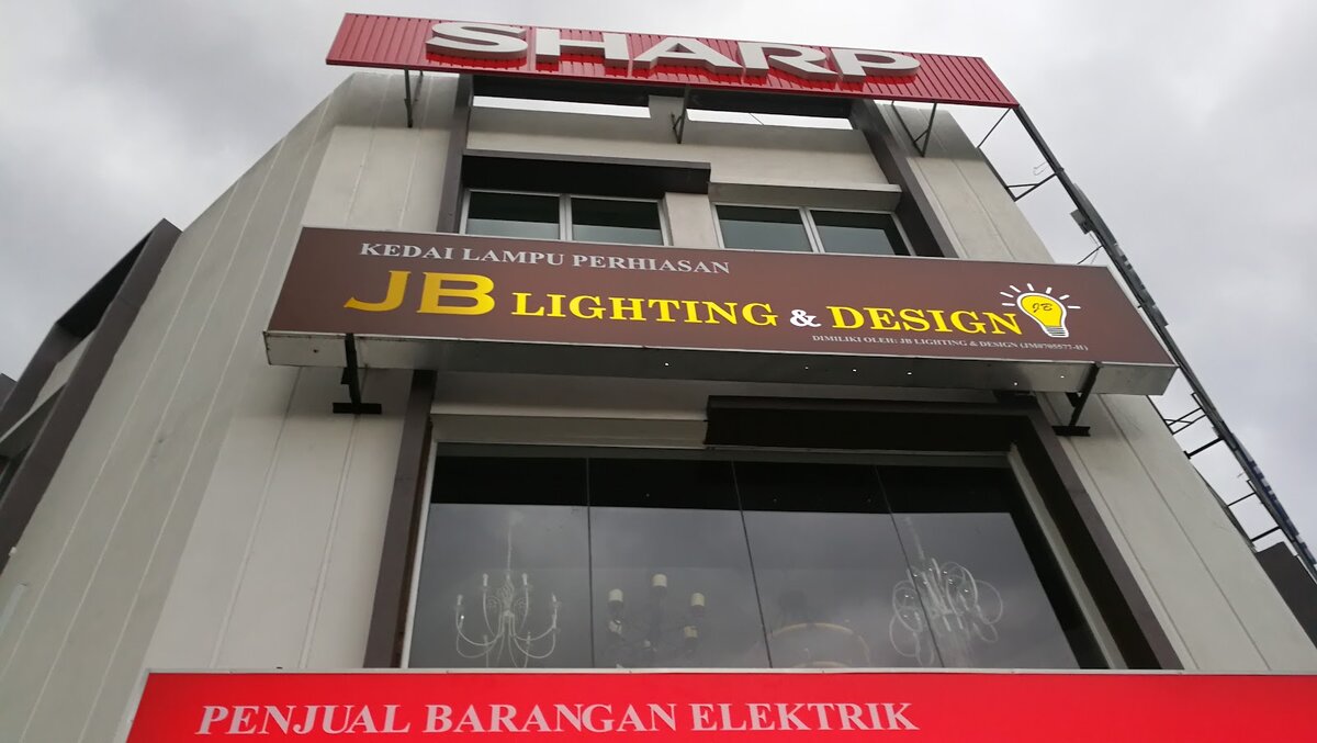 Shophouse with a brown "Kedai Lampu Perhiasan JB Lighting & Design" signboard above a red "Penjual Barangan Elektrik" sign, chandeliers visible behind the upper windows