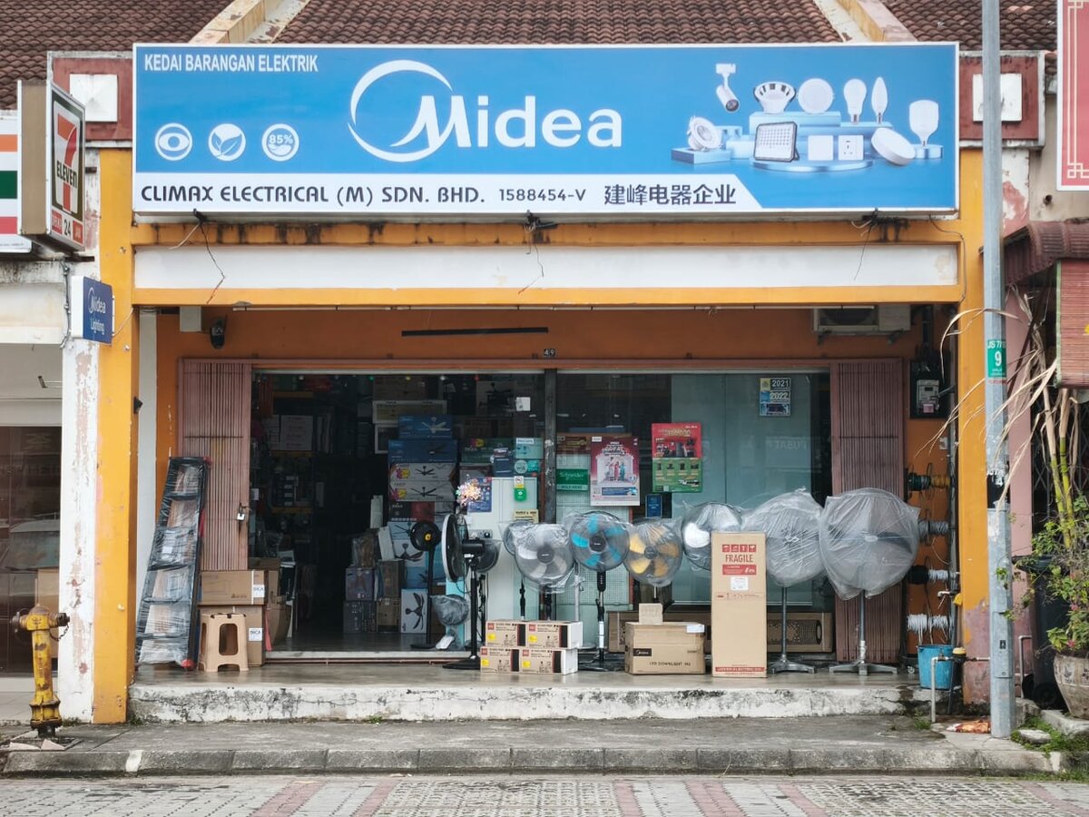 Single shopfront under a blue Midea signboard reading Climax Electrical (M) Sdn. Bhd. and 建峰电器企业, with plastic-wrapped stand fans and boxed stock in front of the open shop
