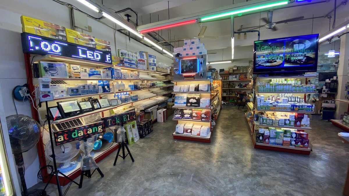 Shop interior with shelves of boxed LED bulbs, floodlights and panels, a CCTV display stand and an LED message board